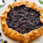 baked blueberry galette on parchment paper with fresh blueberries.