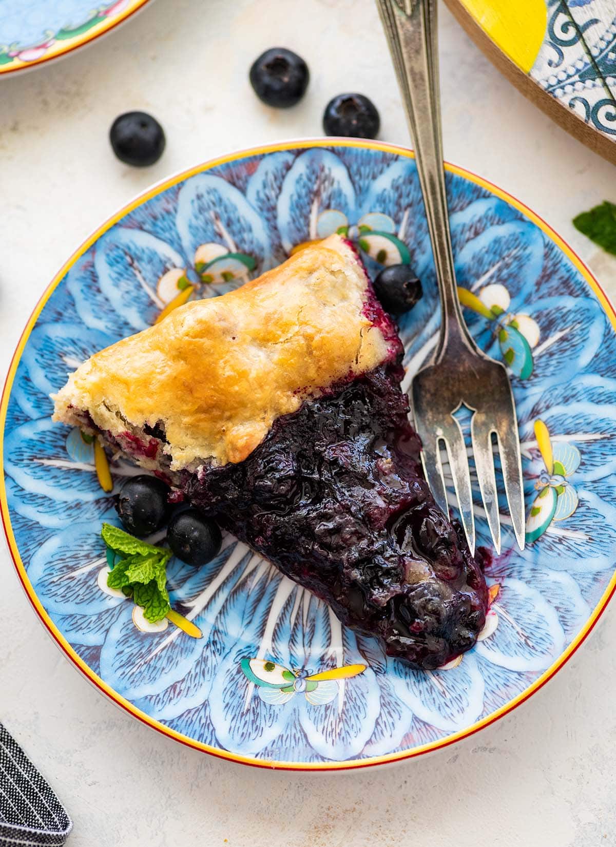 slice of blueberry galette and a fork on a blue floral plate.