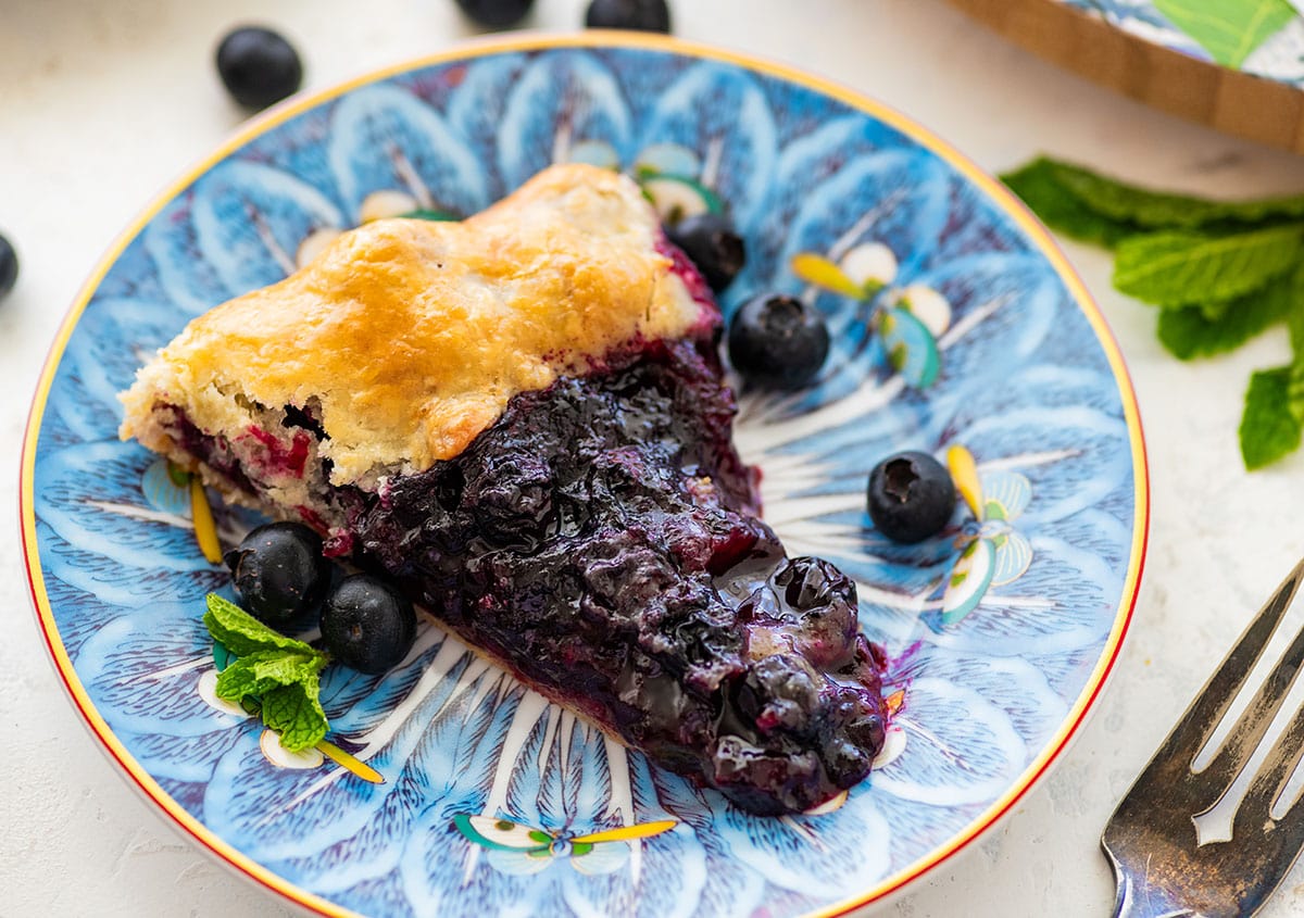 slice of blueberry galette on a blue floral plate with a fork.