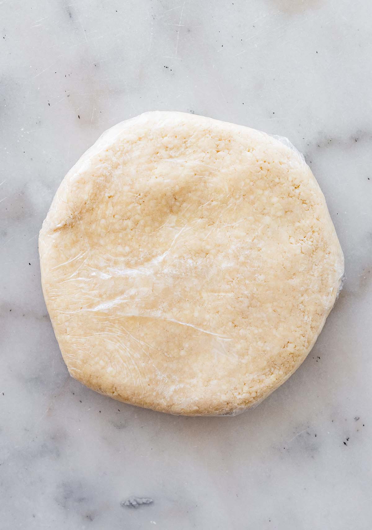 disc of pastry wrapped in plastic on a marble countertop.