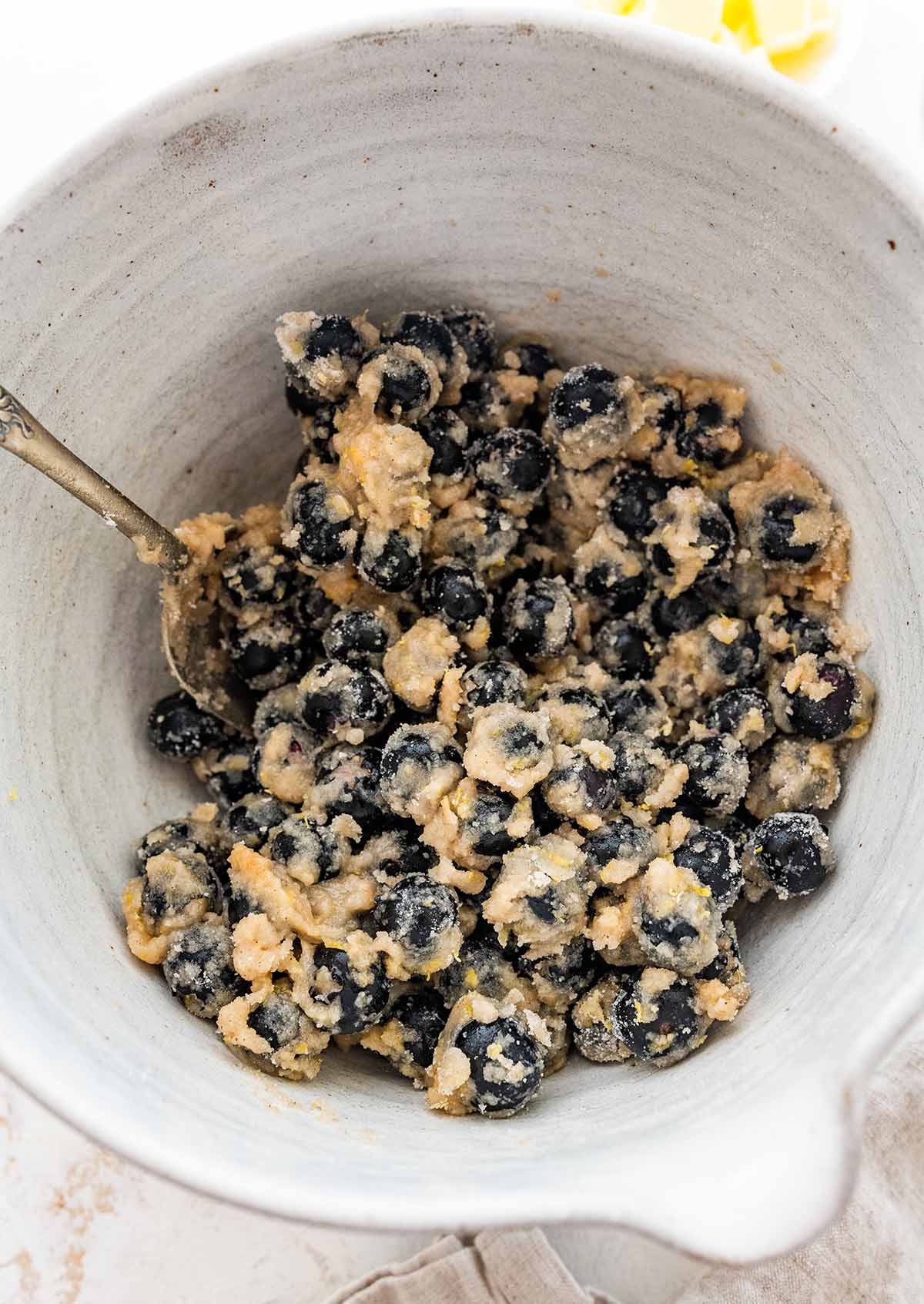 tossing the blueberries with flour and other ingredients in a white bowl.