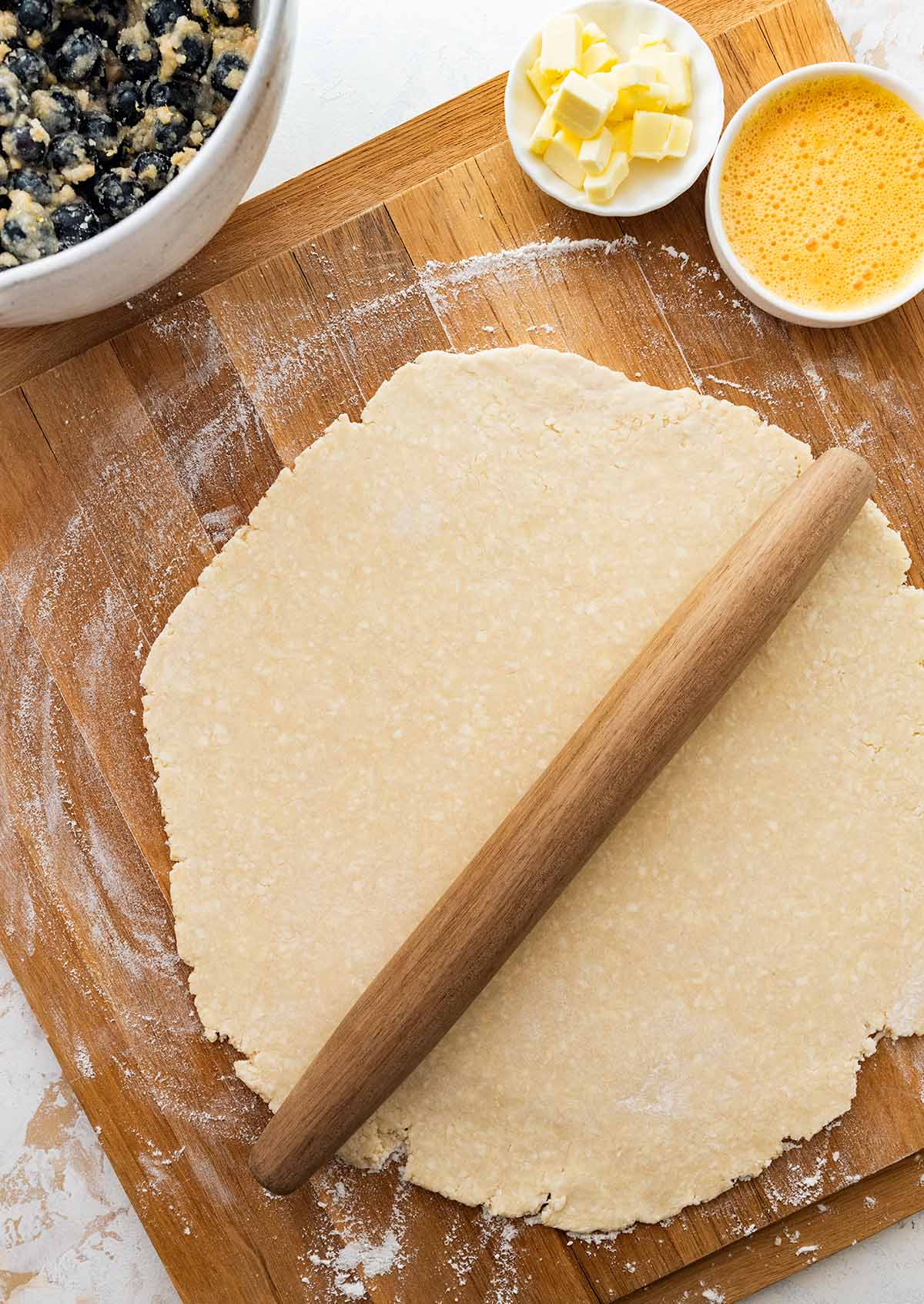 rolling out the pastry on a wooden cutting board.