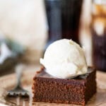 A slice of coca cola cake on a plate with a fork, topped with a scoop of ice cream with more ingredients nearby.
