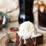 A slice of coca cola cake on a plate with a fork, topped with a scoop of ice cream with more ingredients nearby.