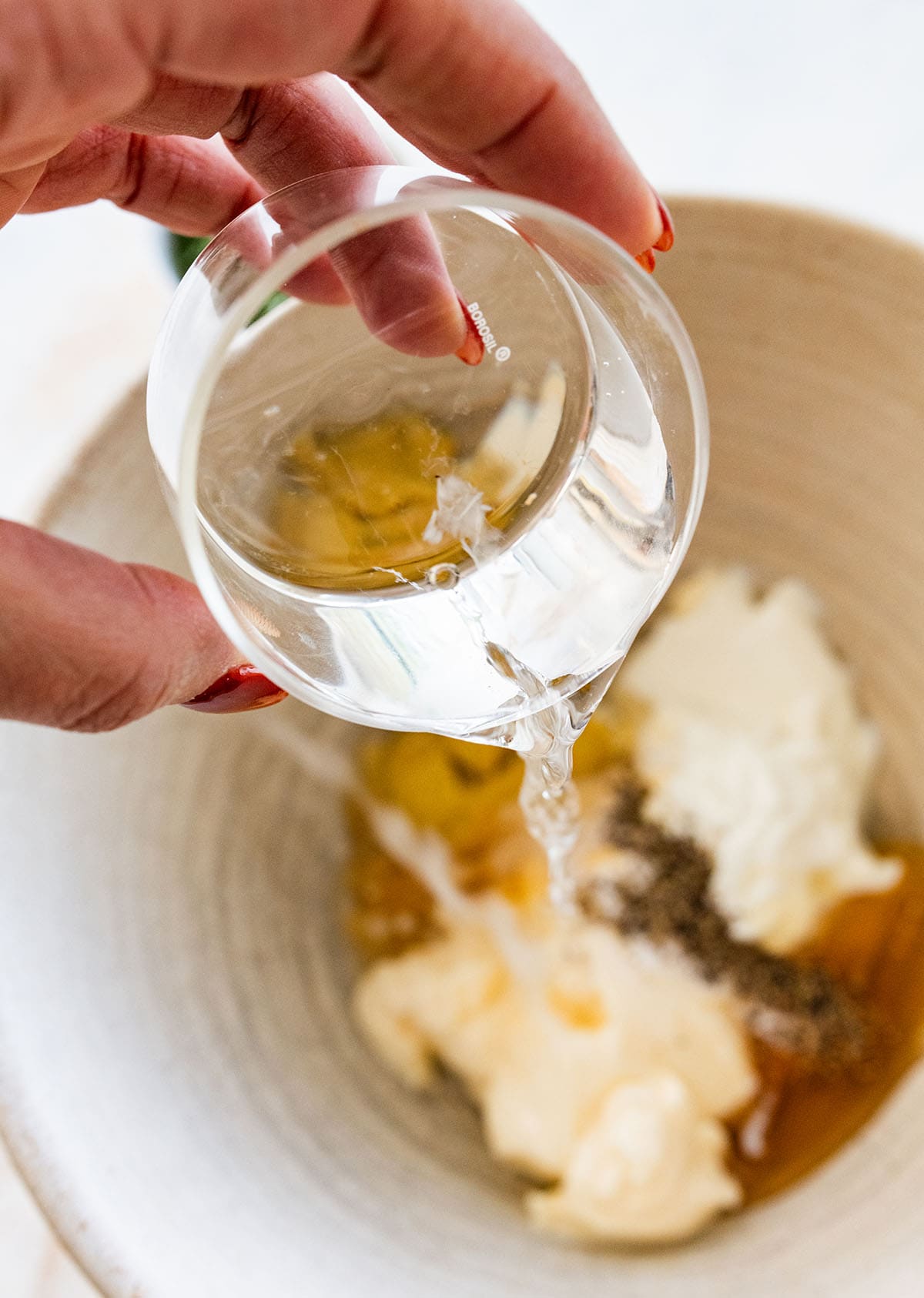 pouring white wine into a bowl of dressing ingredients.