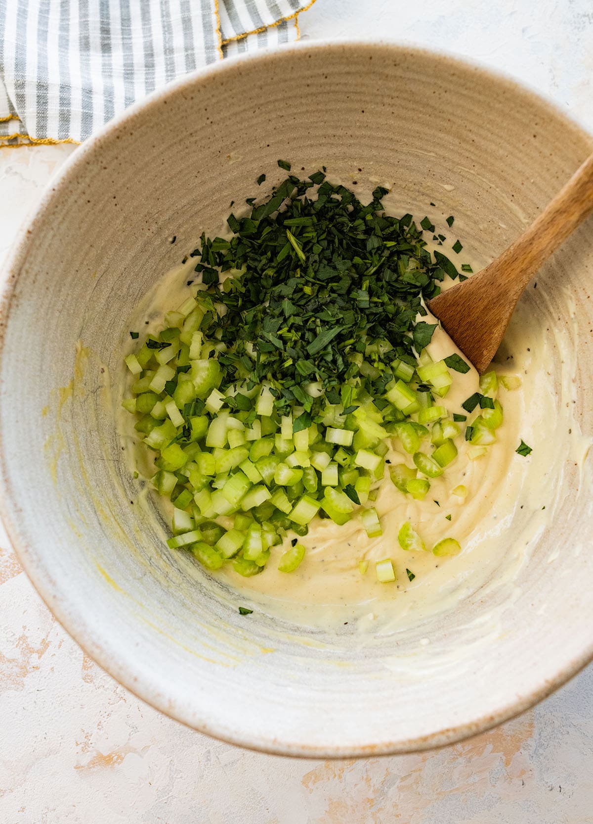 adding diced celery and chopped tarragon into the creamy dressing.
