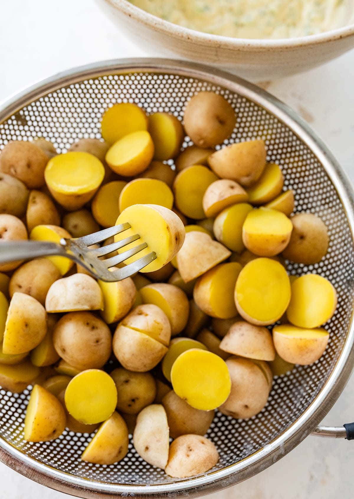 testing small Yukon Gold potatoes with a fork in a strainer.