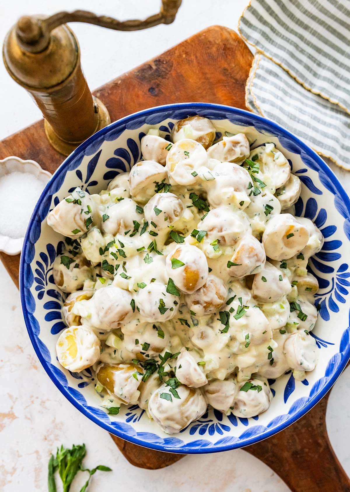 blue and white bowl of creamy potato salad garnished with tarragon.