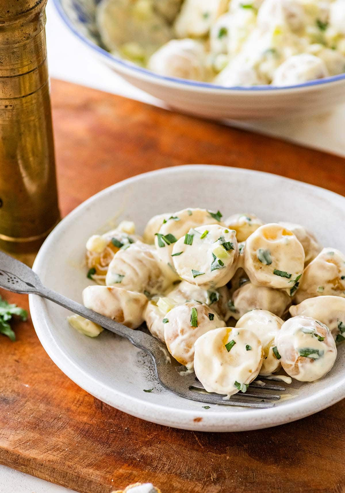 shallow white bowl of creamy potato salad with a fork.