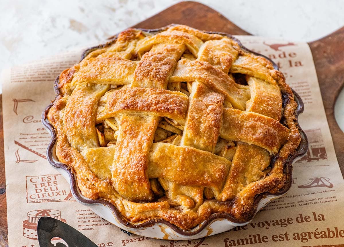 baked lattice-topped apple pie on a newspaper-lined wooden cutting board.