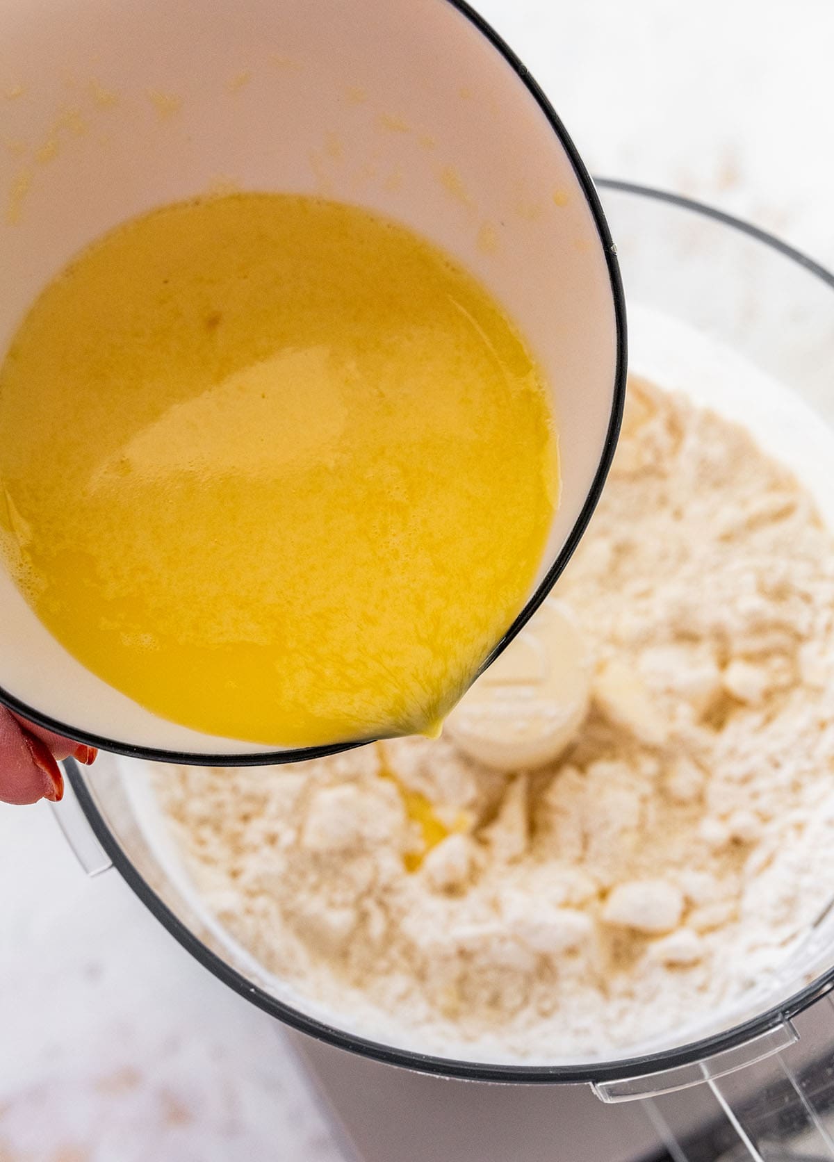 slowly pouring the egg mixture into the flour and butter mixture in the food processor.