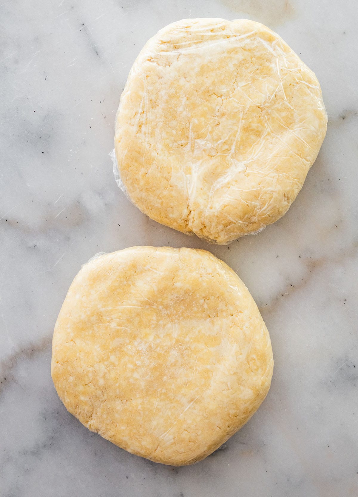 two plastic-wrapped disks of pastry on a marble surface.