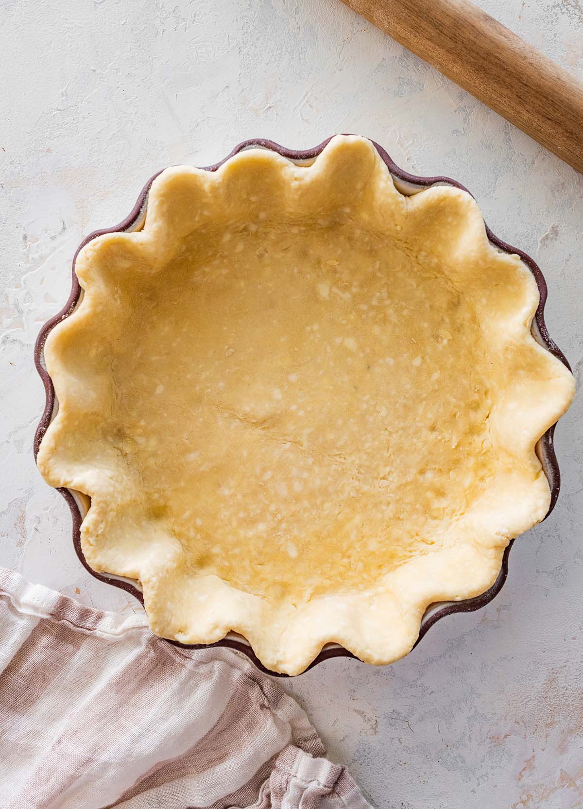 pastry in a deep, fluted pie dish with a rolling pin nearby.