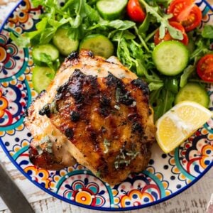 grilled chicken thigh with a side salad and lemon wedge on a colorful plate.
