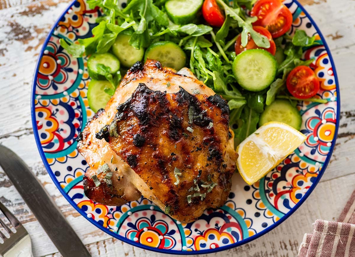 grilled chicken thigh with a side salad and lemon wedge on a colorful plate.