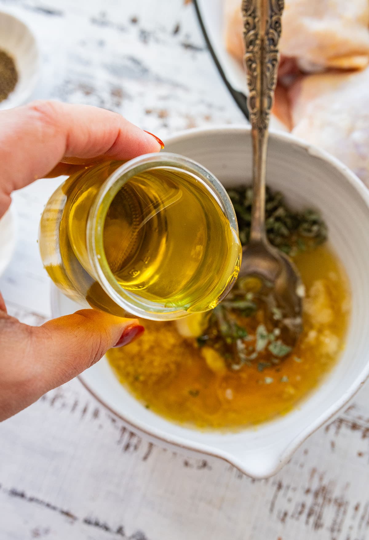 pouring olive oil into a white bowl of chicken marinade.