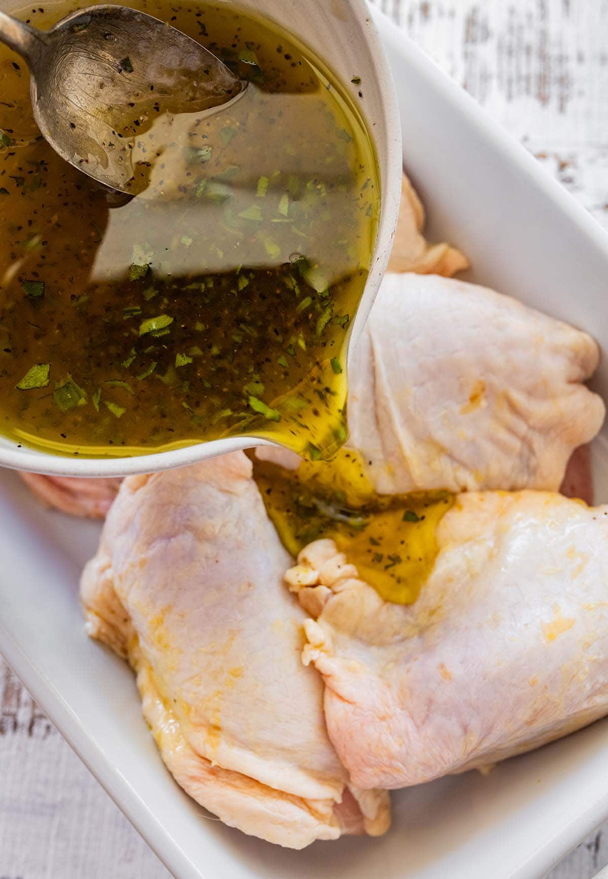 pouring the marinade over bone-in, skin-on chicken thighs in a dish.