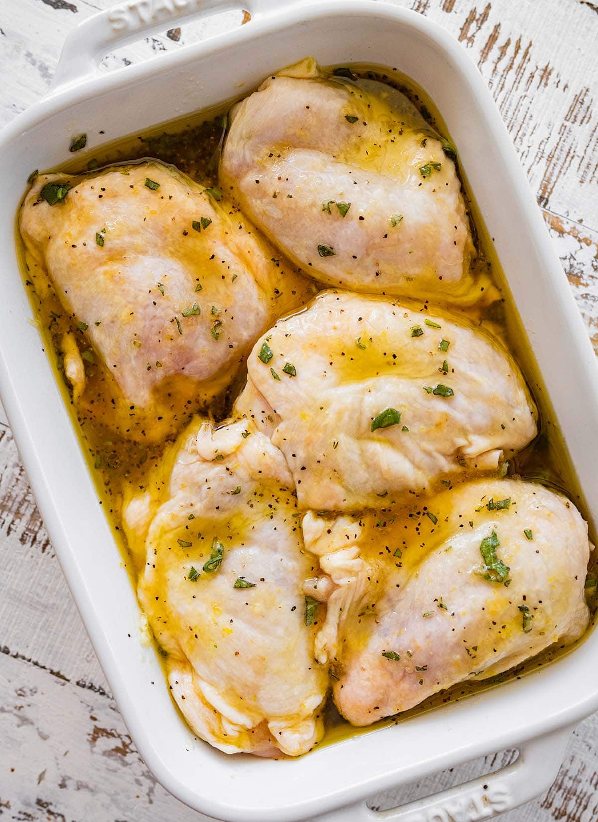 skin-on chicken thighs marinating in a rectangular white dish with handles.