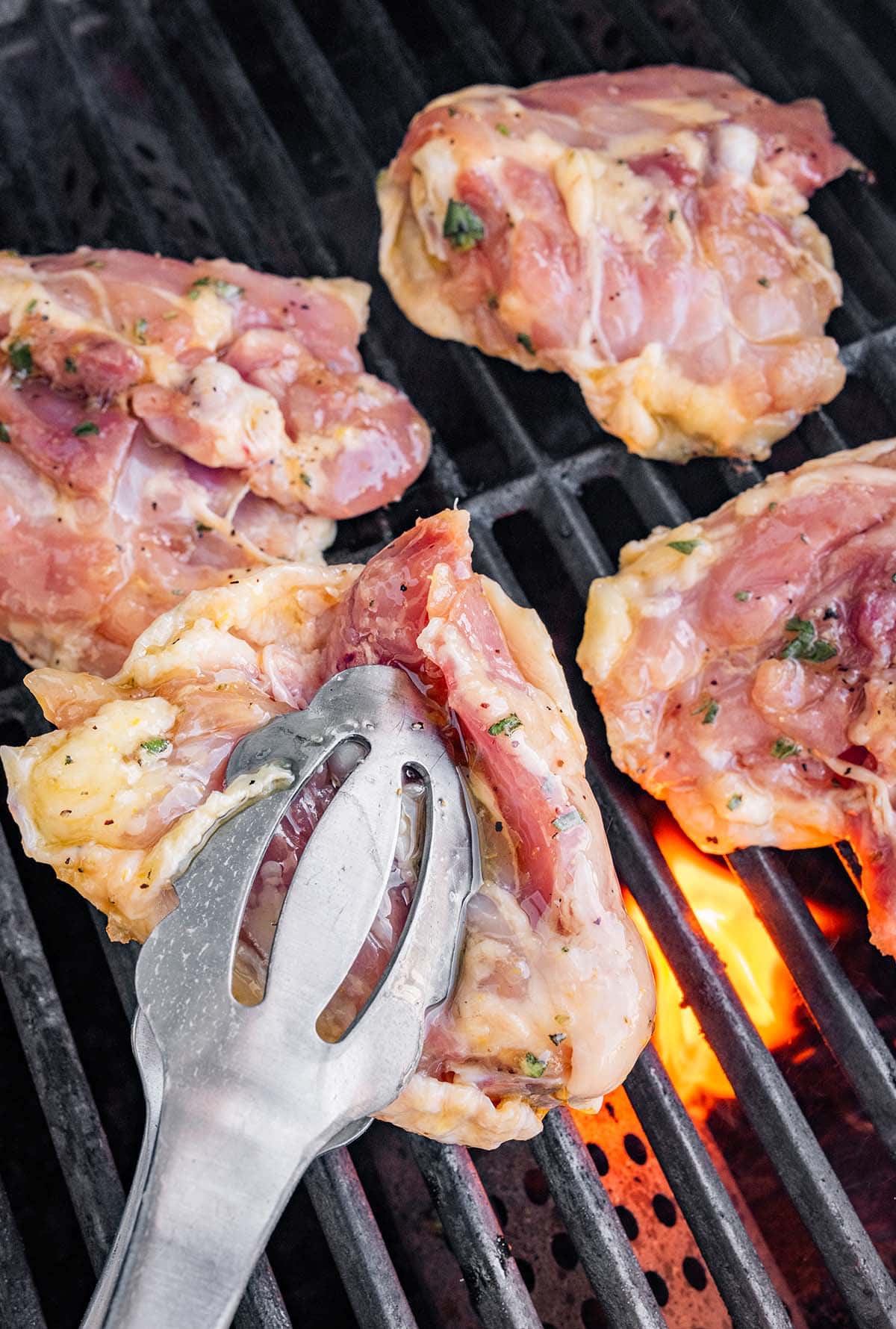 placing marinated chicken thighs on the grill with metal tongs.