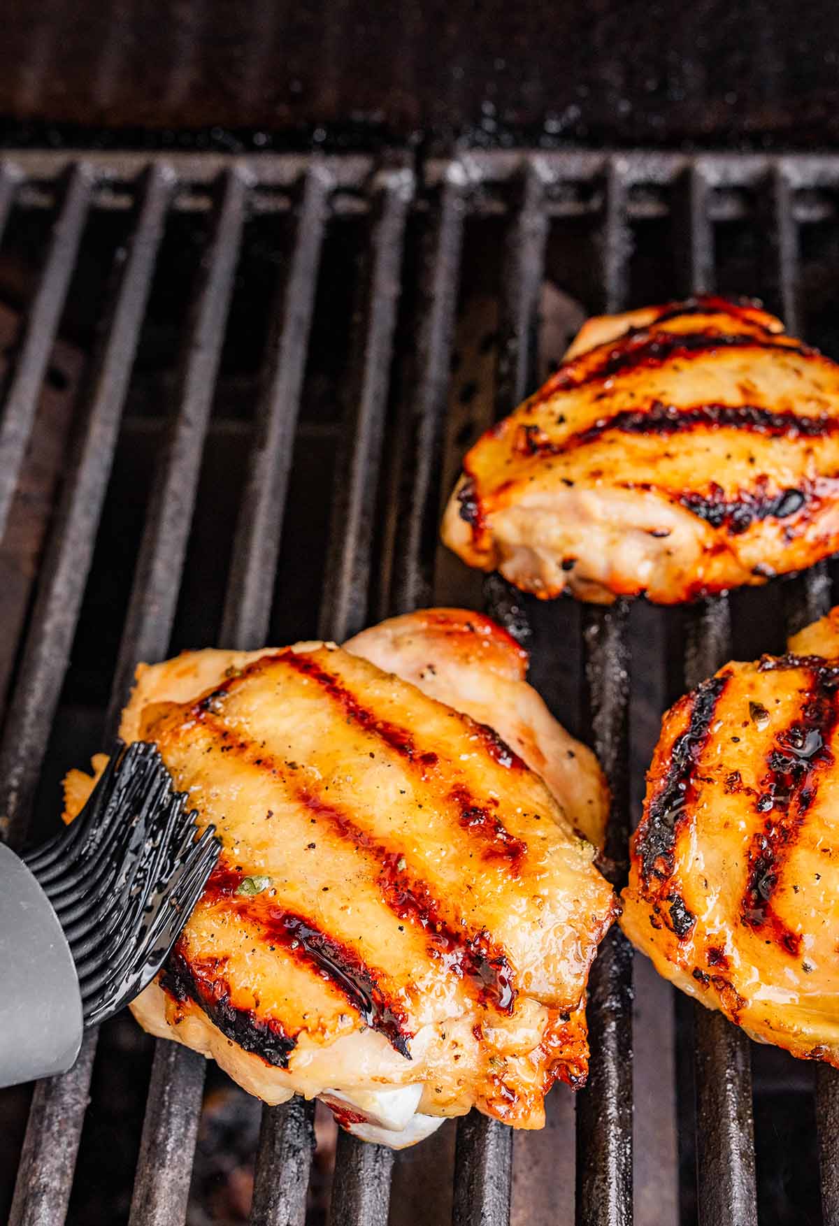 brushing marinade on grilled chicken with sear marks.