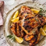 stack of grilled chicken thighs with lemon wedges and fresh sage.