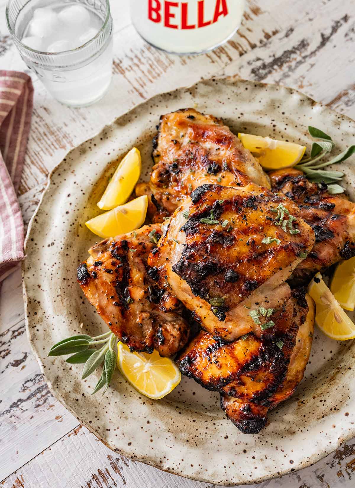 stack of grilled chicken thighs with lemon wedges and fresh sage.