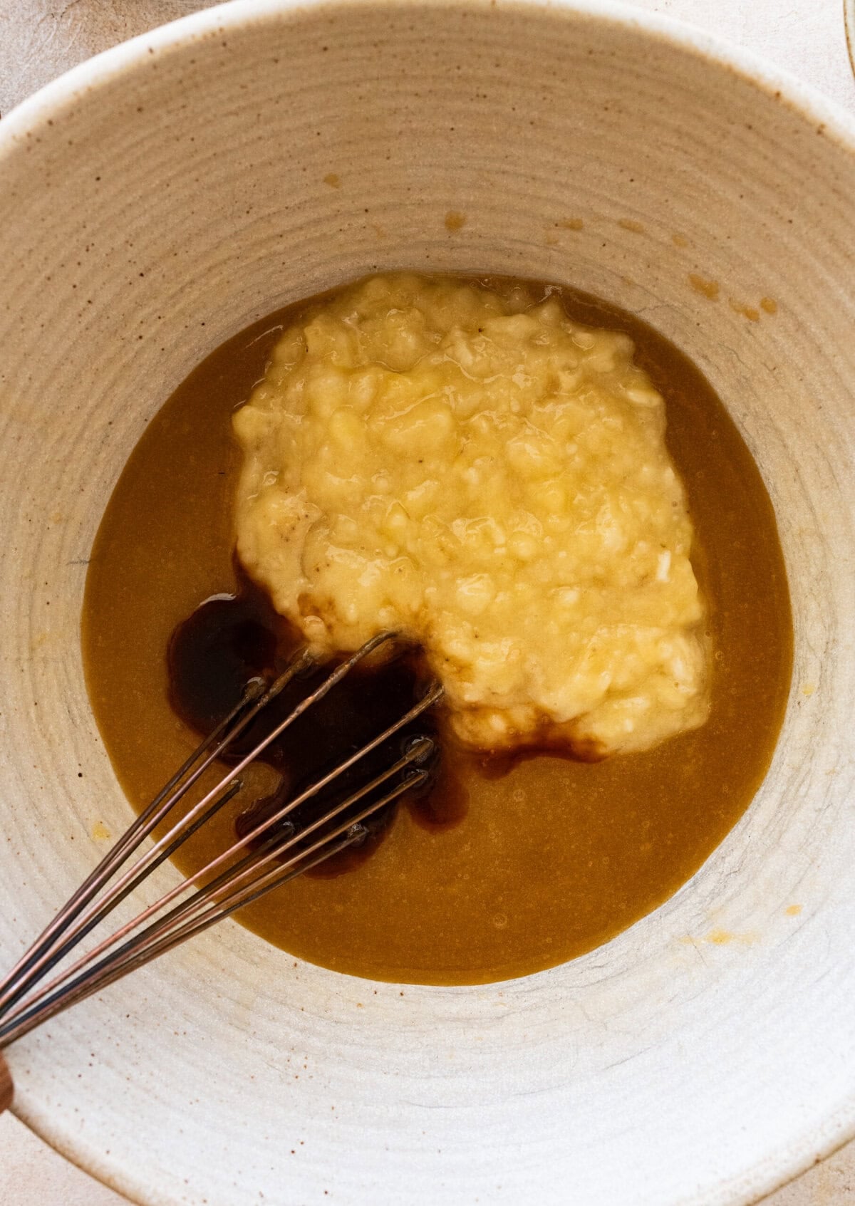 Mashed banana and vanilla added to the bowl, with a whisk resting inside the bowl.