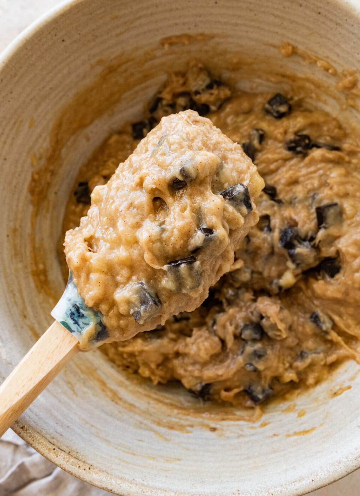 A spatula holding up a scoop of dough over the bowl of dough.