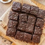 Cut brownies on parchment paper with more ingredients nearby.