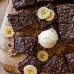 Sliced banana brownies placed on parchment paper with some banana slices around them and one scoop of ice cream on a brownie.