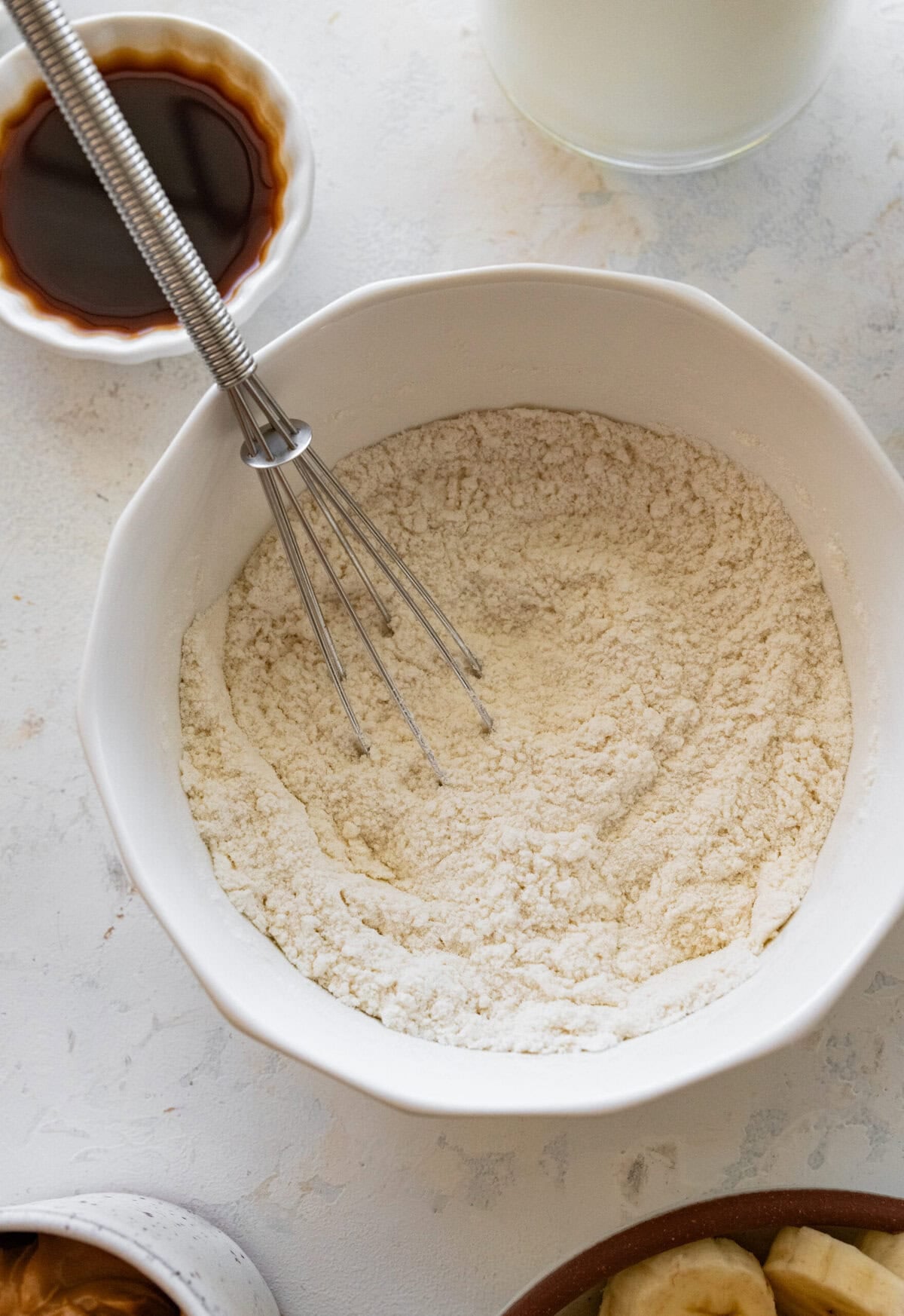 Sugar, flour, and salt in a bowl with a whisk resting inside and more ingredients nearby.