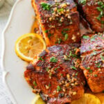 Blackened salmon garnished with parsley plated with lemon wedges.