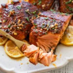 Blackened salmon garnished with parsley plated with lemon wedges with a fork holding up a bite.