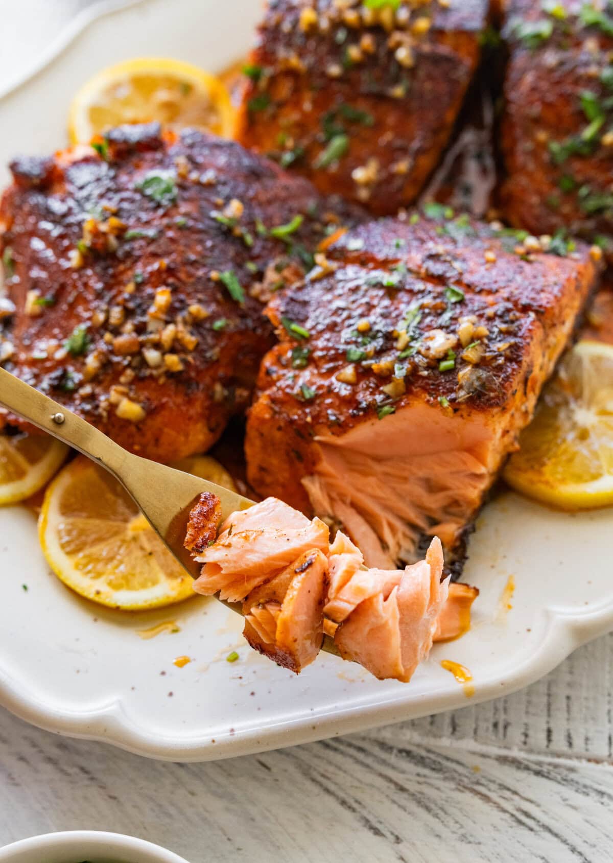 Blackened salmon garnished with parsley plated with lemon wedges with a fork holding up a bite.