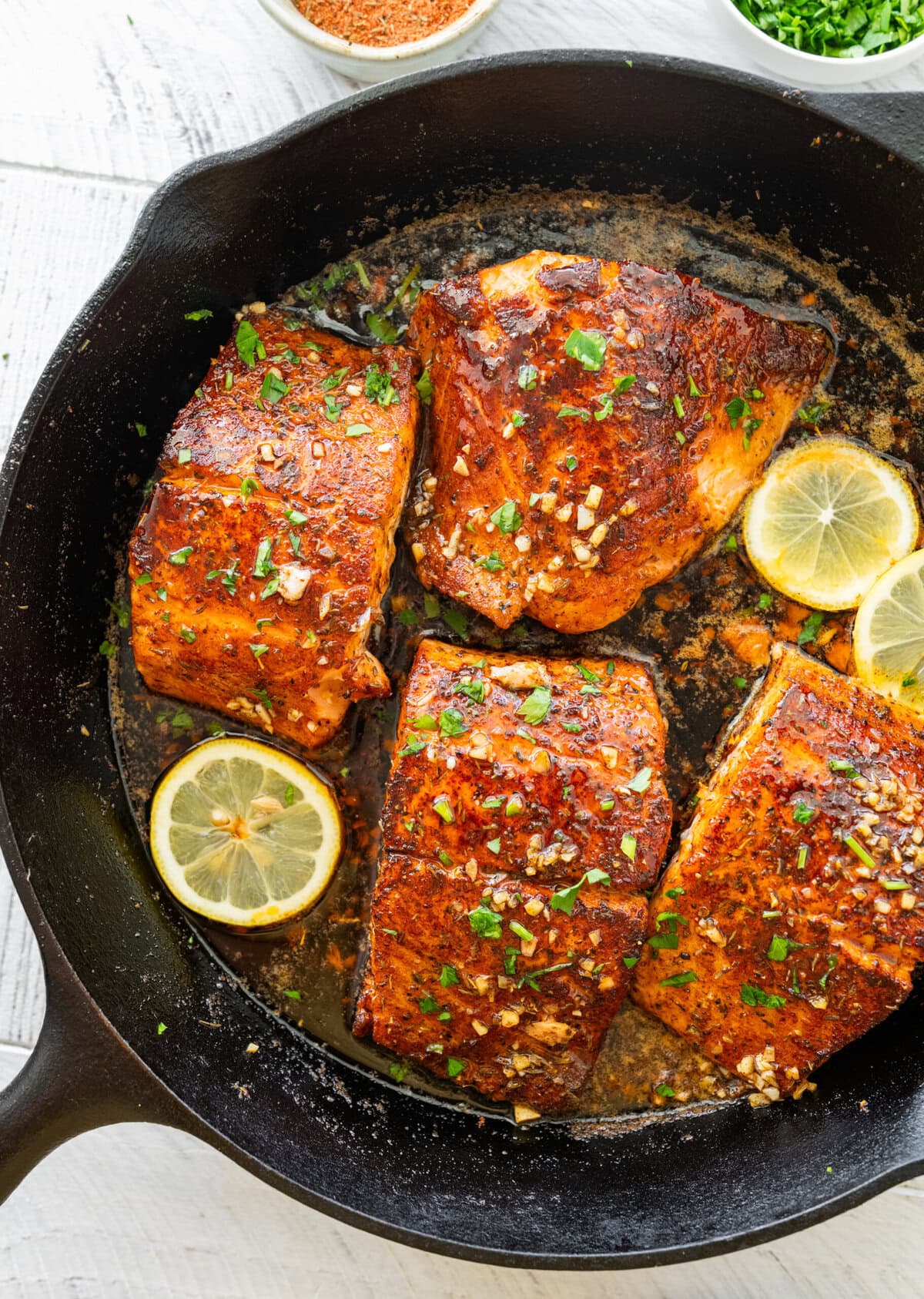 Salmon in a skillet with lemon slices and parsley.