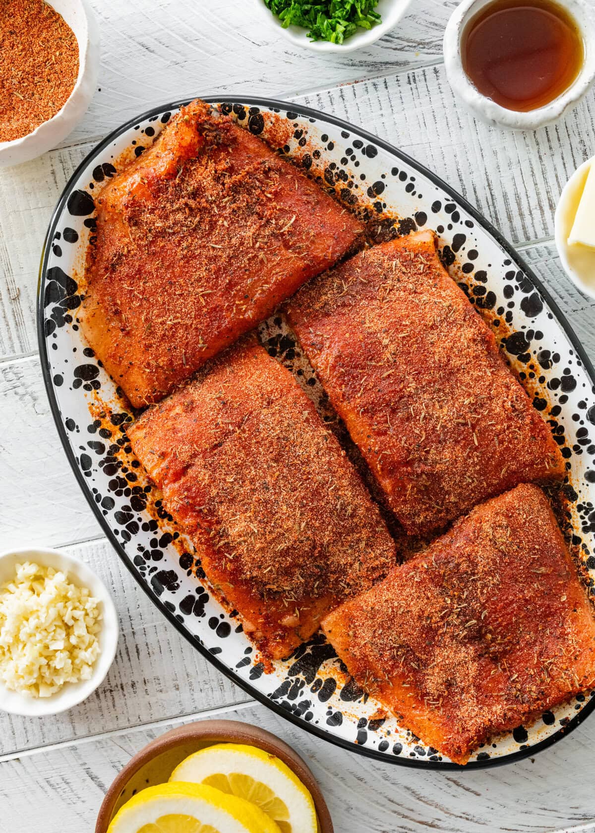 Salmon on a plate with the blackening seasoning on top, and more ingredients nearby.