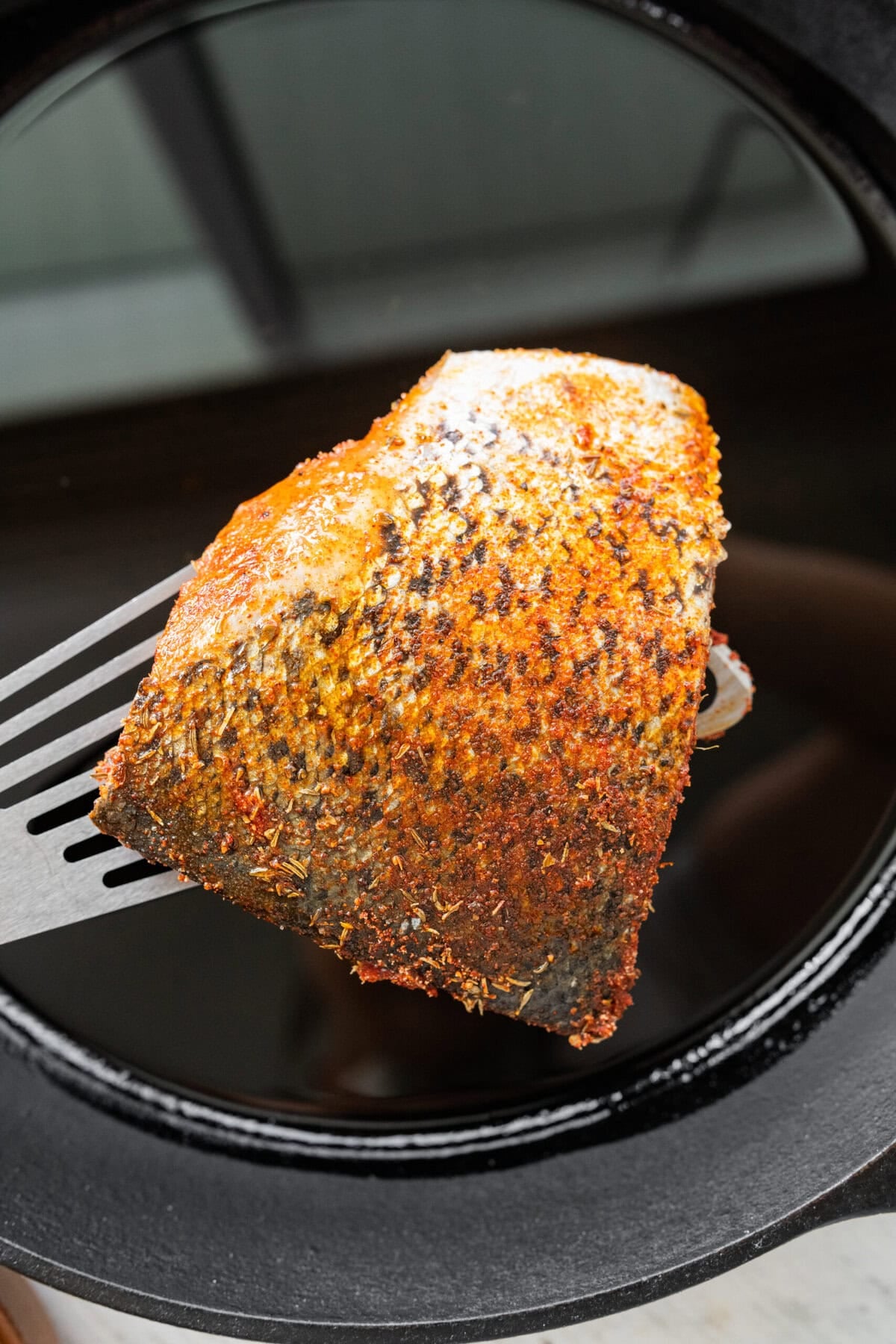 A piece of salmon being lowered over a cast iron pan.
