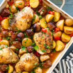 A baking dish of chicken scarpariello after cooking, with more ingredients nearby.
