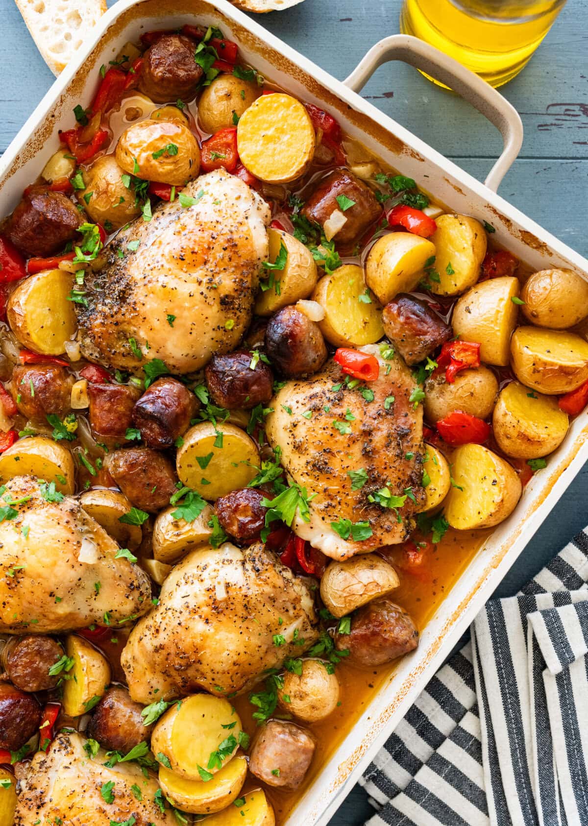 A baking dish of chicken scarpariello after cooking, with more ingredients nearby.