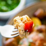 A fork holding up a bite of chicken over a plate of more.