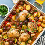 A baking dish of chicken scarpariello after cooking, with more ingredients nearby.