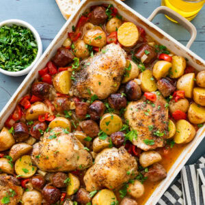 A baking dish of chicken scarpariello after cooking, with more ingredients nearby.