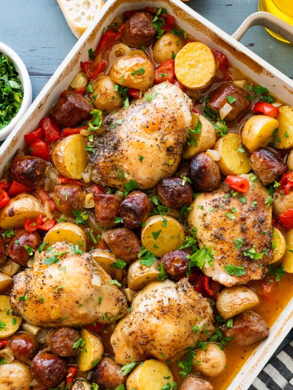 A baking dish of chicken scarpariello after cooking, with more ingredients nearby.