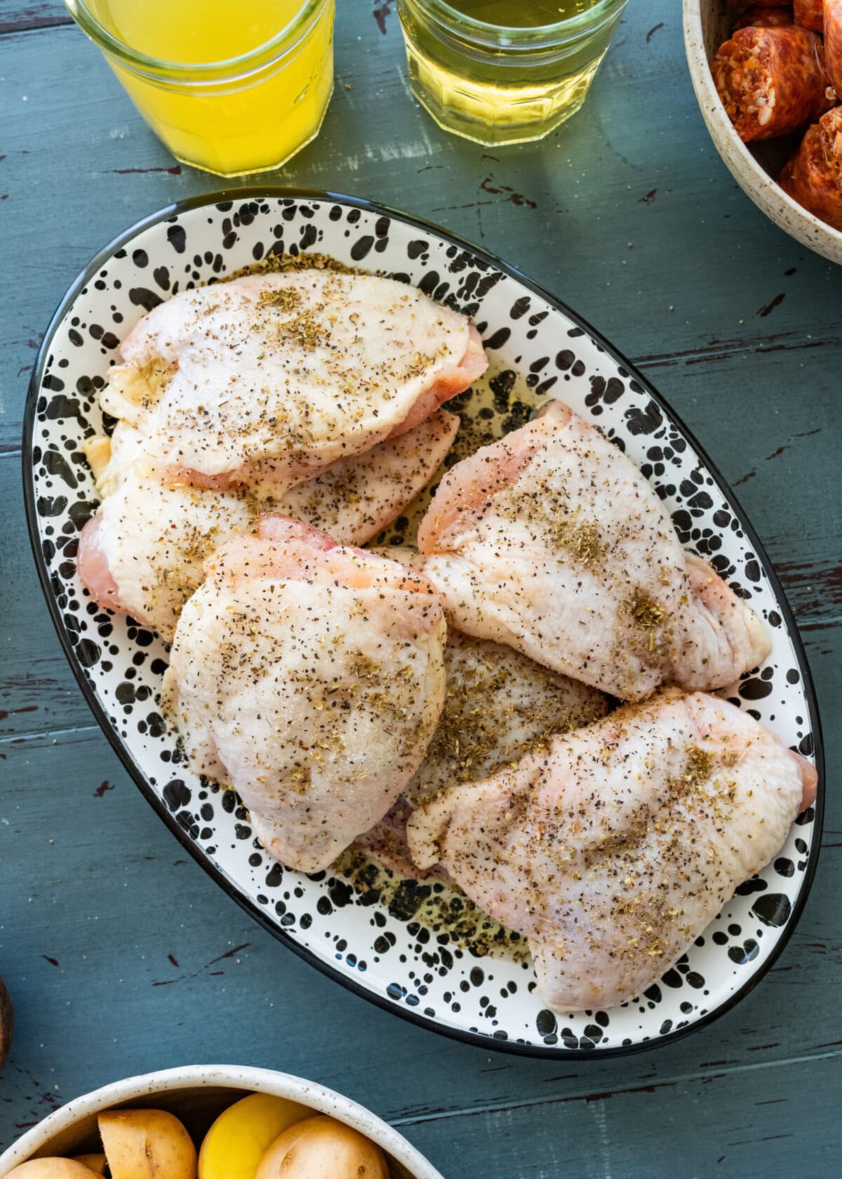 Seasoned chicken thighs on a plate with more ingredients nearby. 