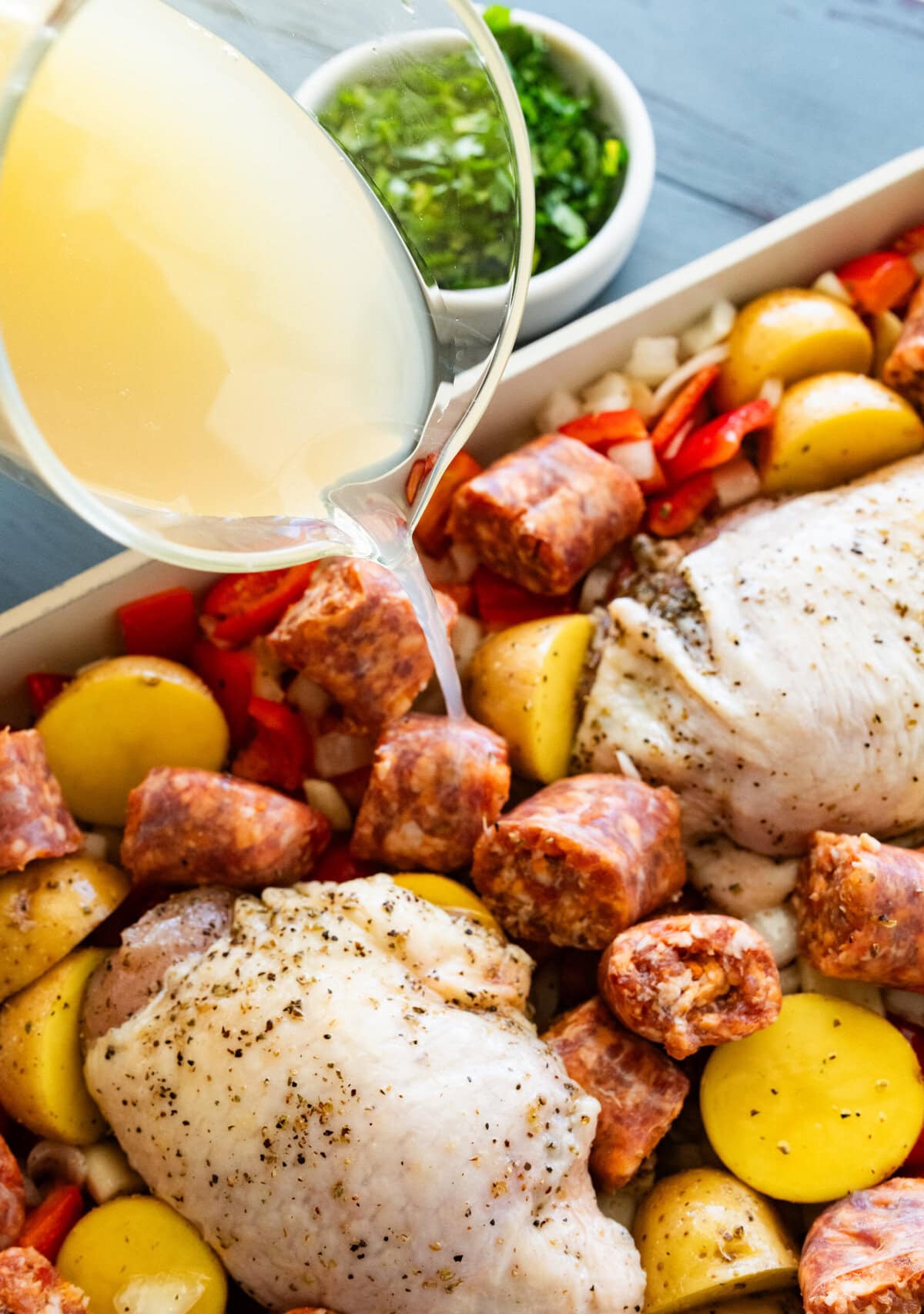 A cup with the white wine, white wine vinegar, and chicken stock being poured over the veggies. 