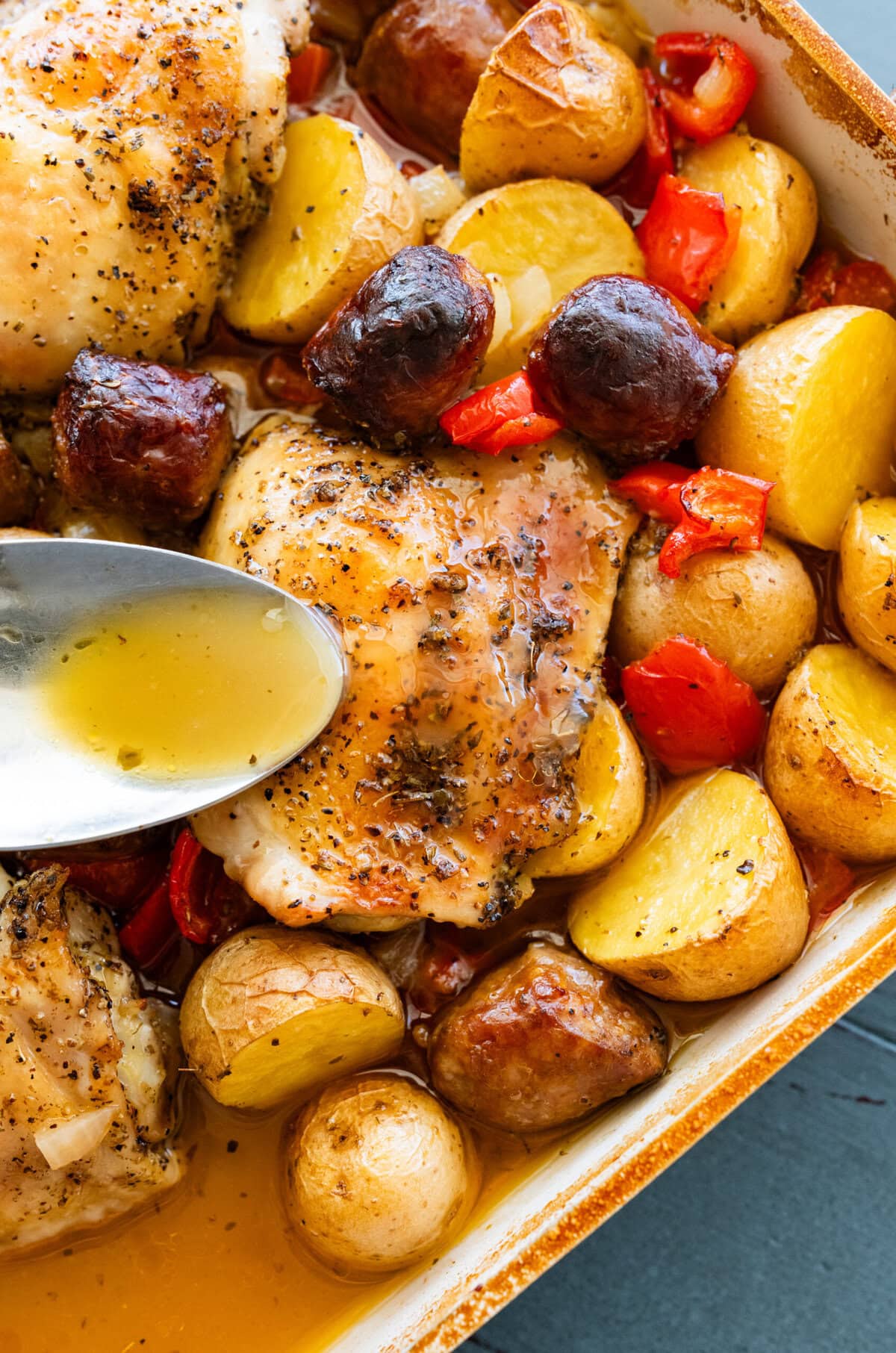 A spoon pouring some sauce over the edges of the chicken and veggies.
