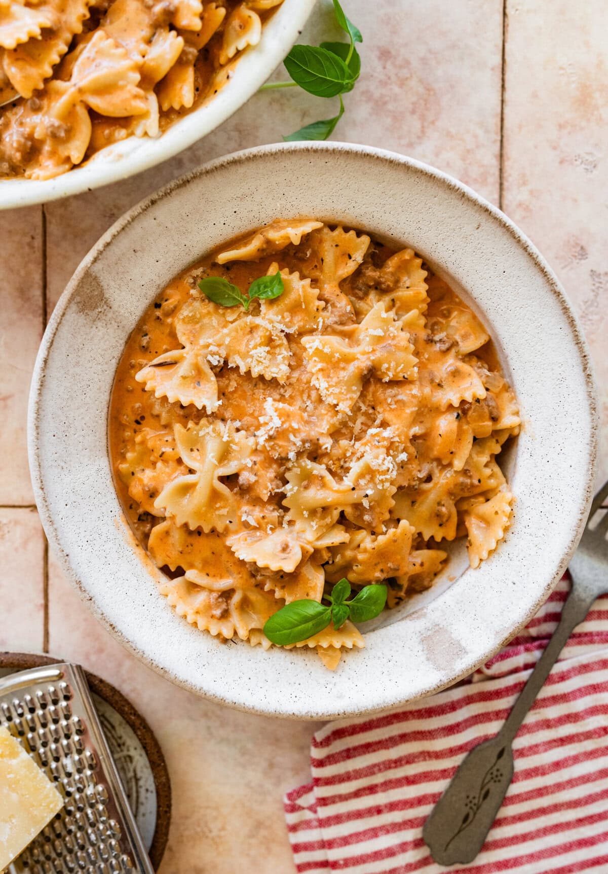 A large bowl of beef and bowtie pasta with a smaller bowl nearby, topped with basil as garnish.