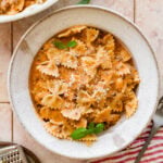 A large bowl of beef and bowtie pasta with a smaller bowl nearby, topped with basil as garnish.