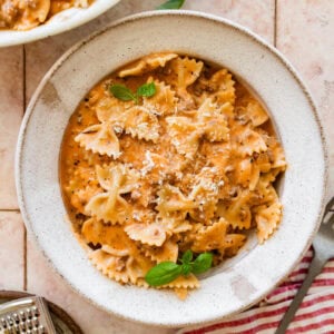 A large bowl of beef and bowtie pasta with a smaller bowl nearby, topped with basil as garnish.