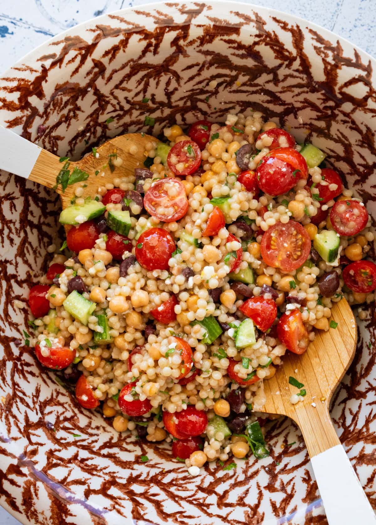 Two utensils resting in a bowl of pearl couscous salad after mixing.